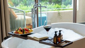 A modern bathroom with a freestanding bathtub, a tray with fruits and a glass of wine, and a view of greenery outside. - Zen Valley Dalat (Xuan Huong - Da Lat)