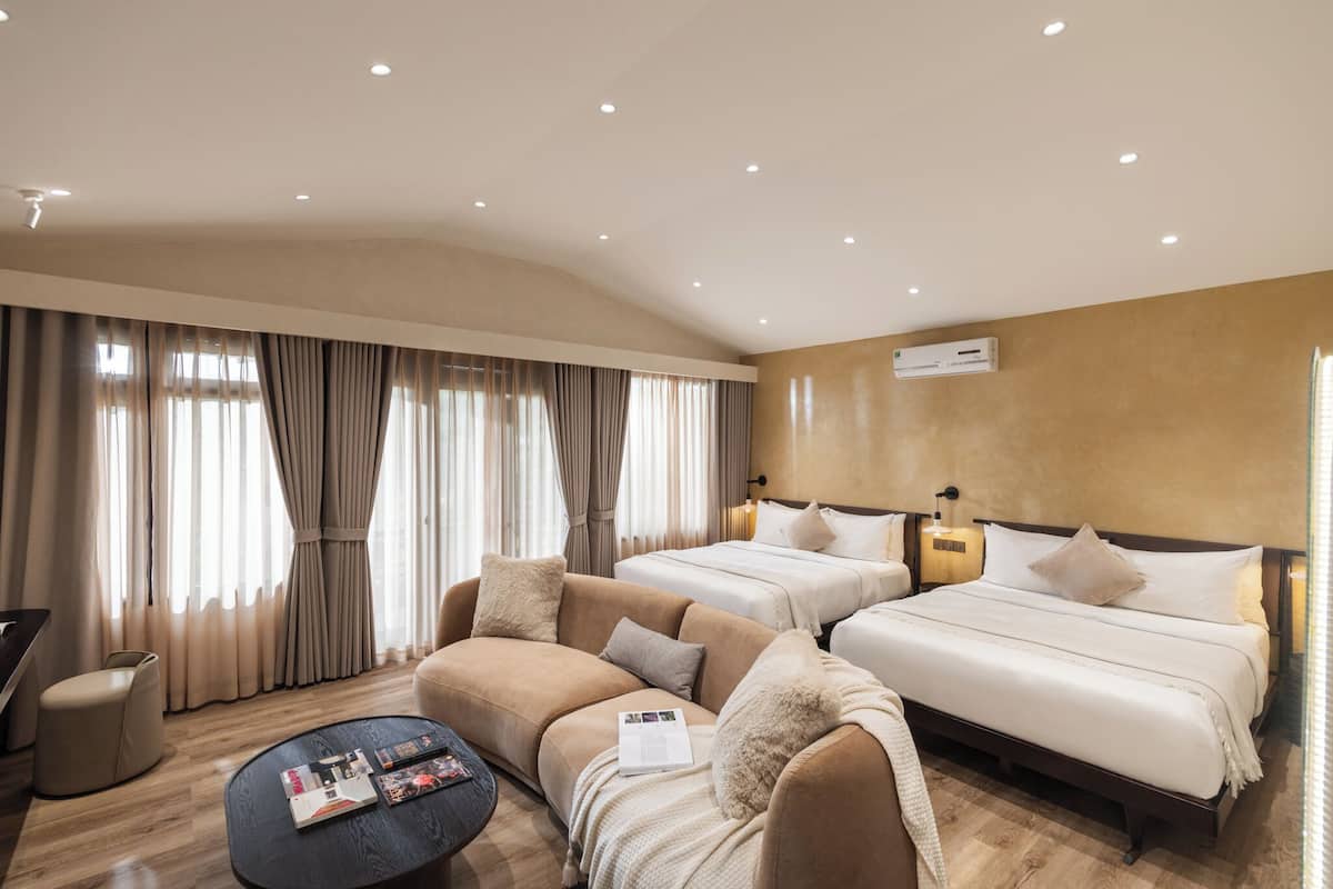A hotel room with two beds, a sofa, a coffee table, and a large window with curtains.