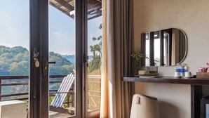 A hotel room with a balcony, a desk with a mirror, a heater, and a view of a forested area. - Zen Valley Dalat (Xuan Huong - Da Lat)