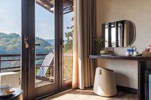A hotel room with a balcony, a desk with a mirror, a heater, and a view of a forested area. - Zen Valley Dalat (Da Lat)