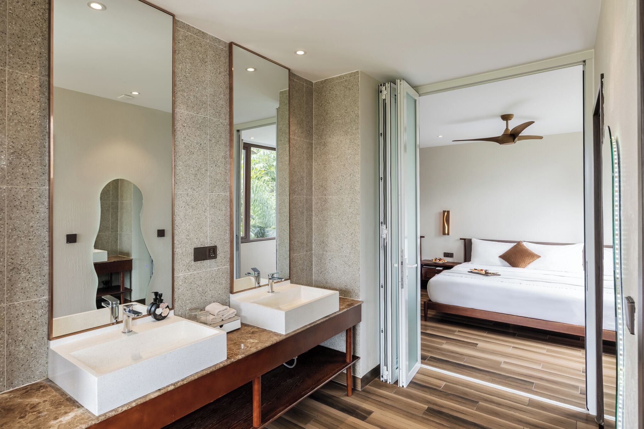 Una habitación de hotel moderna con dos lavamanos, un espejo grande, un ventilador de techo y una cama con vistas.