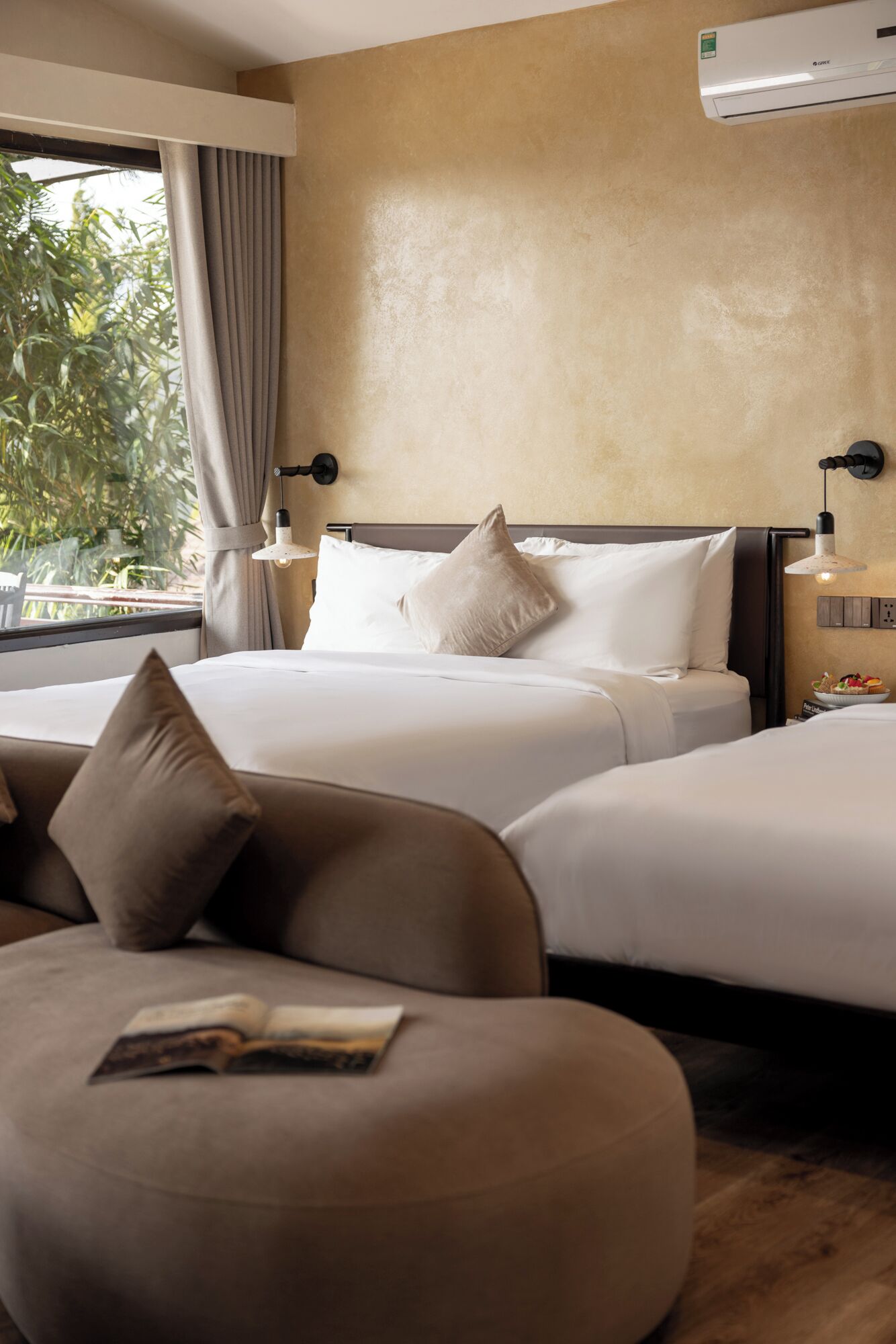 Ein Hotelzimmer mit einem Bett, zwei Nachttischen, einer Leseecke mit Sofa und Buch sowie einem Fenster mit Vorhängen.