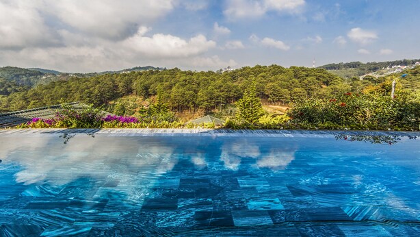 A clear blue infinity pool with a view of a lush green landscape and distant hills. - Zen Valley Dalat (Xuan Huong - Da Lat)