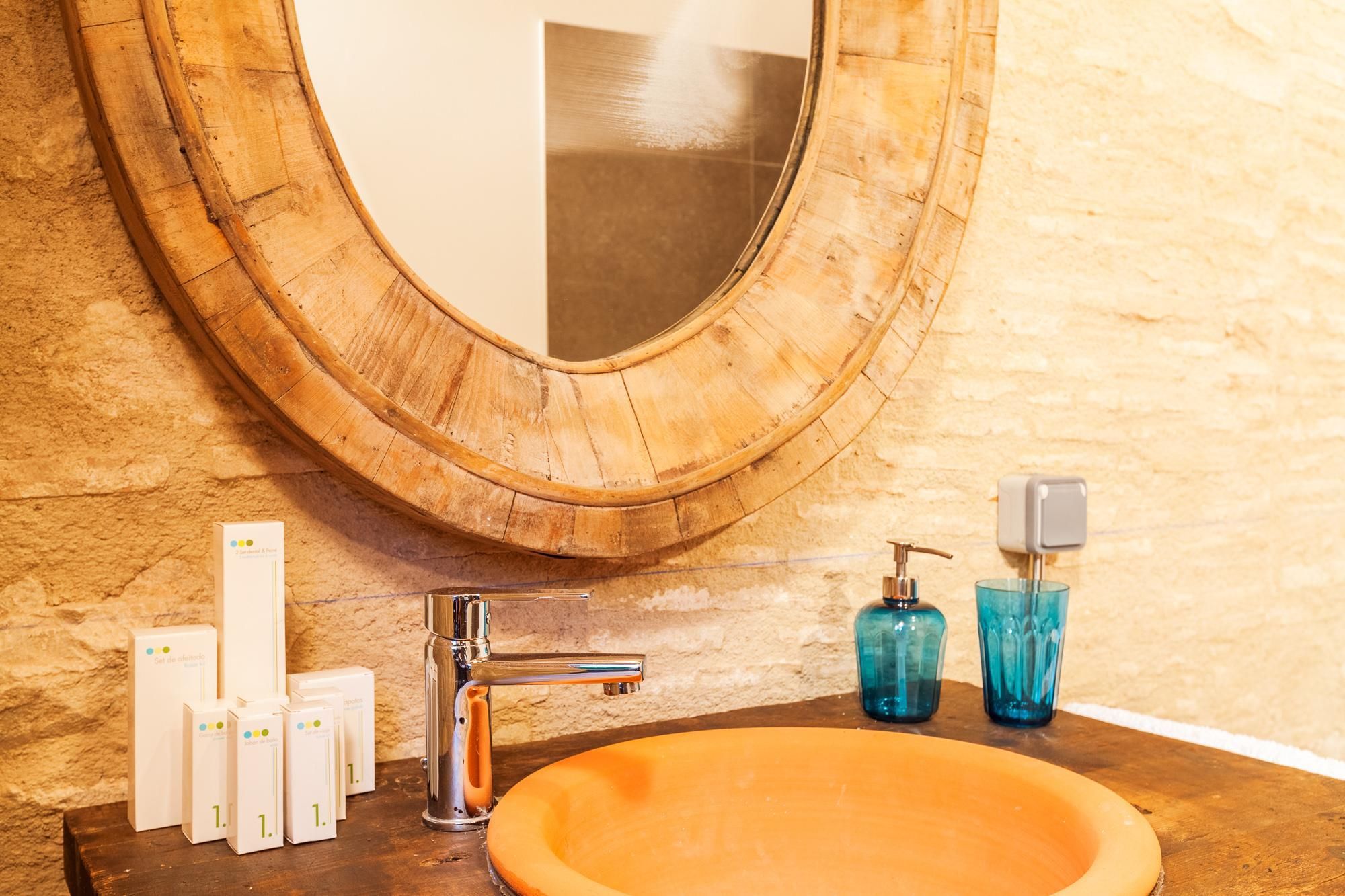 Un baño con un espejo de marco de madera, un grifo moderno y un lavamanos redondo color naranja.