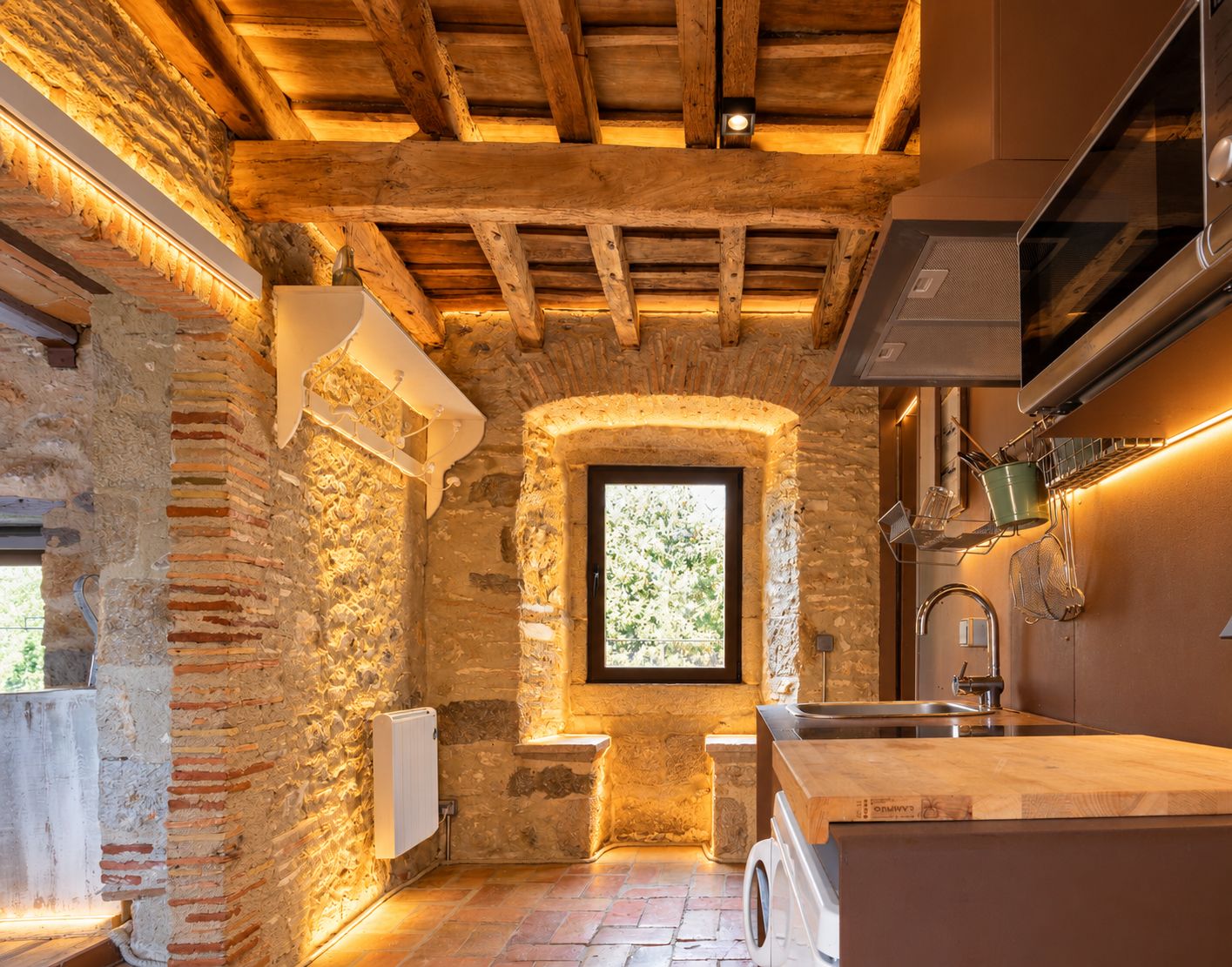 Una cocina rústica con vigas de madera a la vista, una pared de piedra, una ventana y un horno empotrado.
