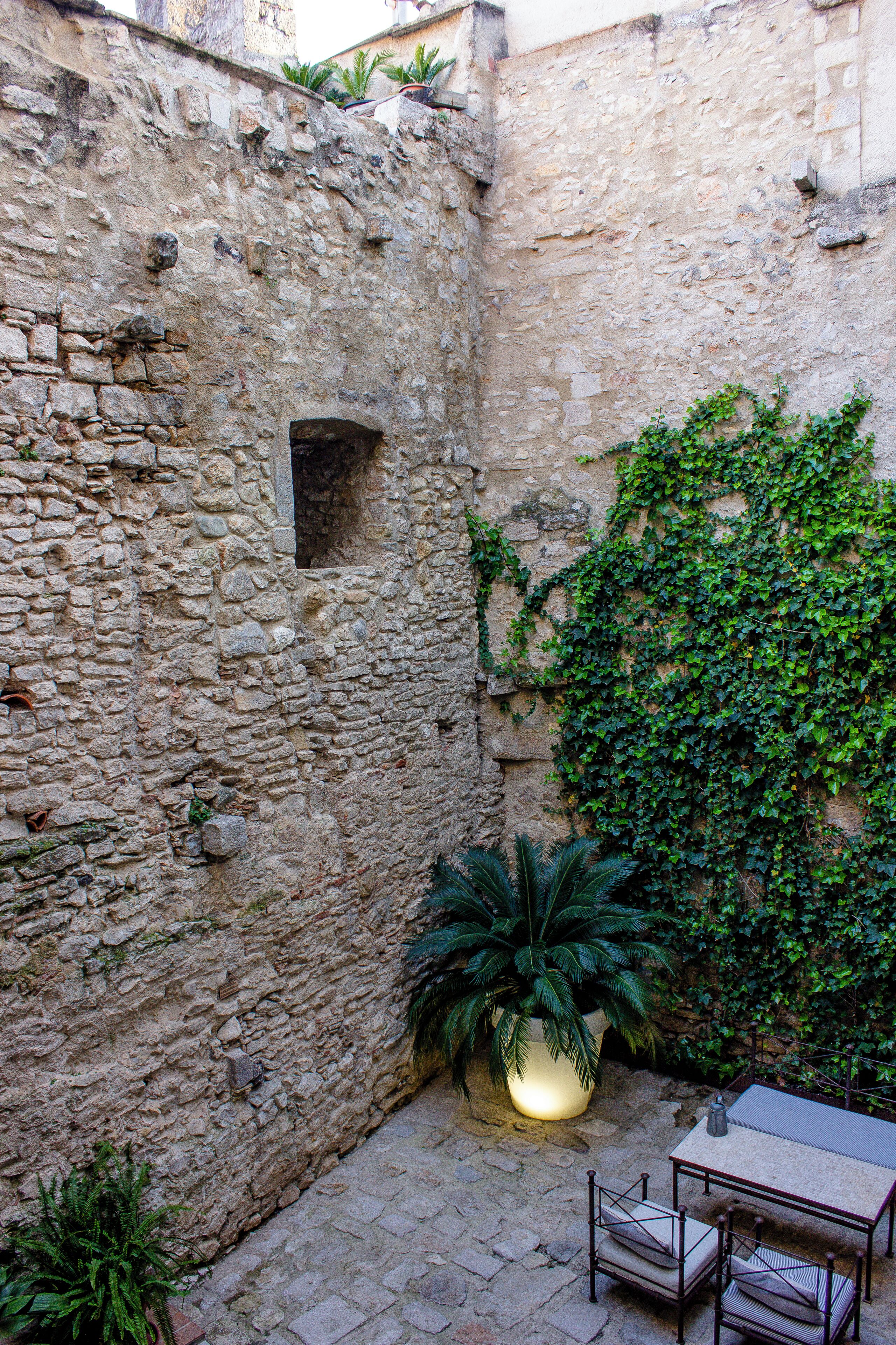 Un patio de piedra con una mesa y sillas, una planta en maceta e una pared cubierta de hiedra.