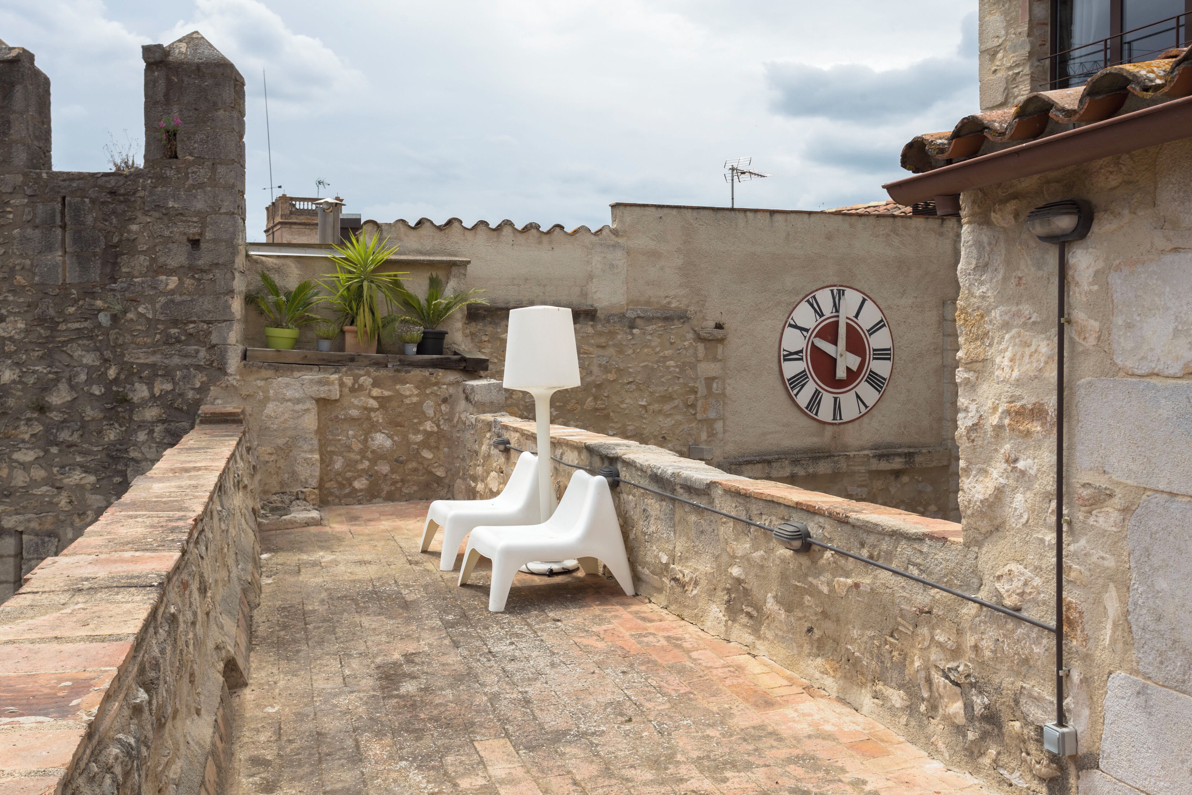 A rooftop terrace with stone walls, a clock, and potted plants.