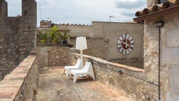 A rooftop terrace with stone walls, a clock, and potted plants.