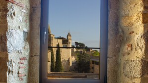Una habitación con paredes de piedra y una ventana con vista a un edificio histórico.
