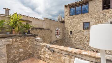 A courtyard with stone walls, a clock, potted plants, and a white table.