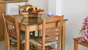 A kitchen with a dining table set for four, a white tiled backsplash, and a small window with curtains. - Maganas Hotel (Astypalaia)