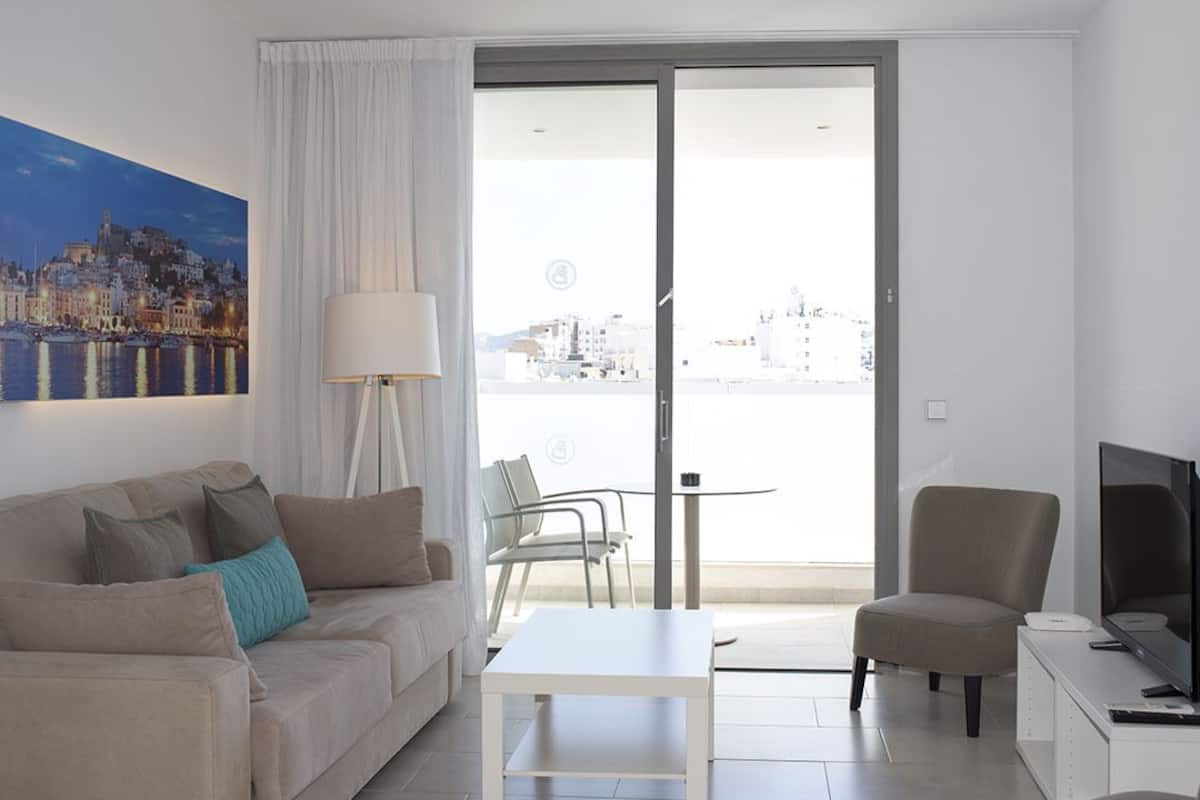 A modern living room with a sofa, a coffee table, a TV, and a balcony with a city view.