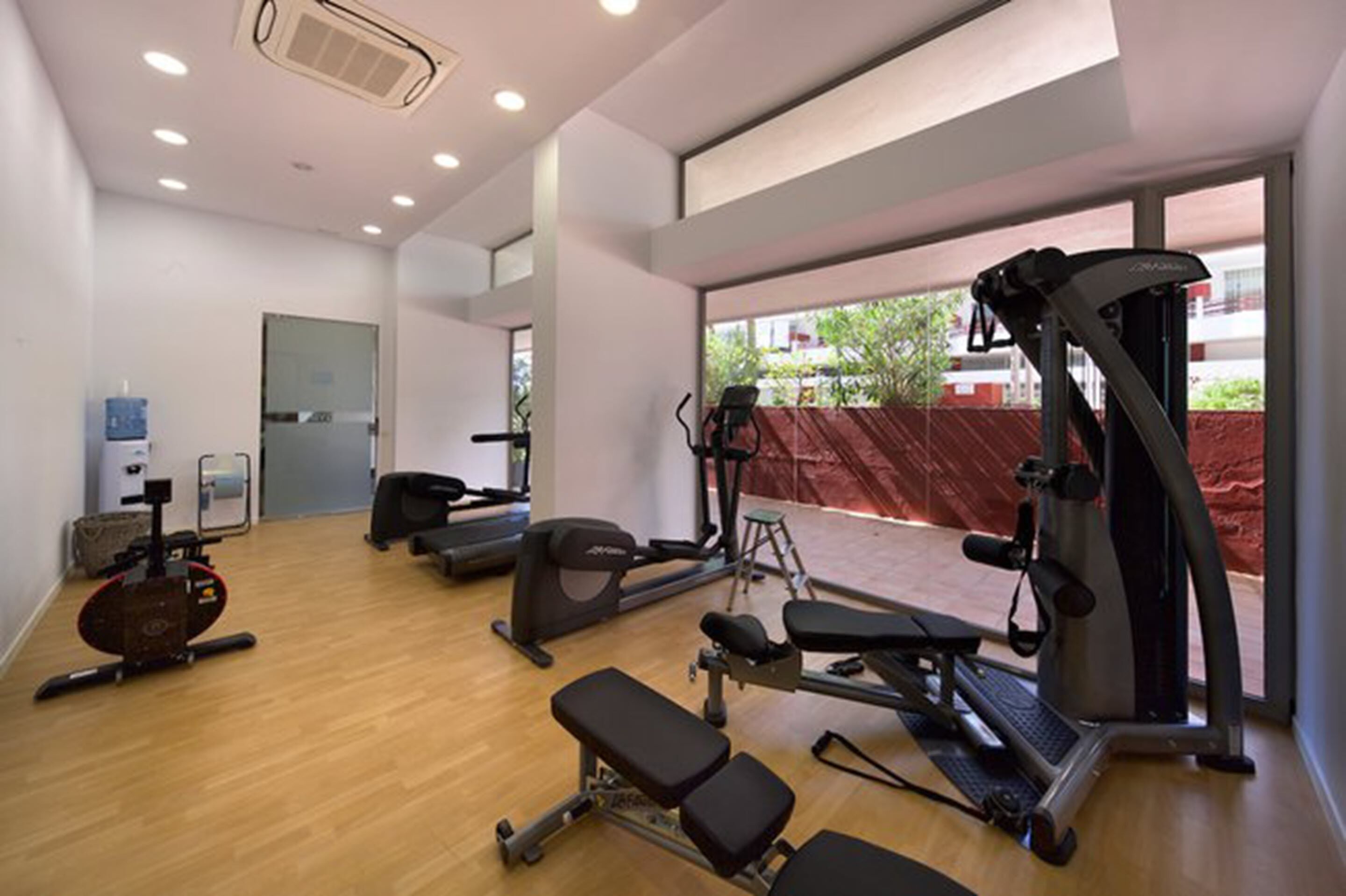Un gimnasio con máquinas de cardio, una banca y un dispensador de agua.
