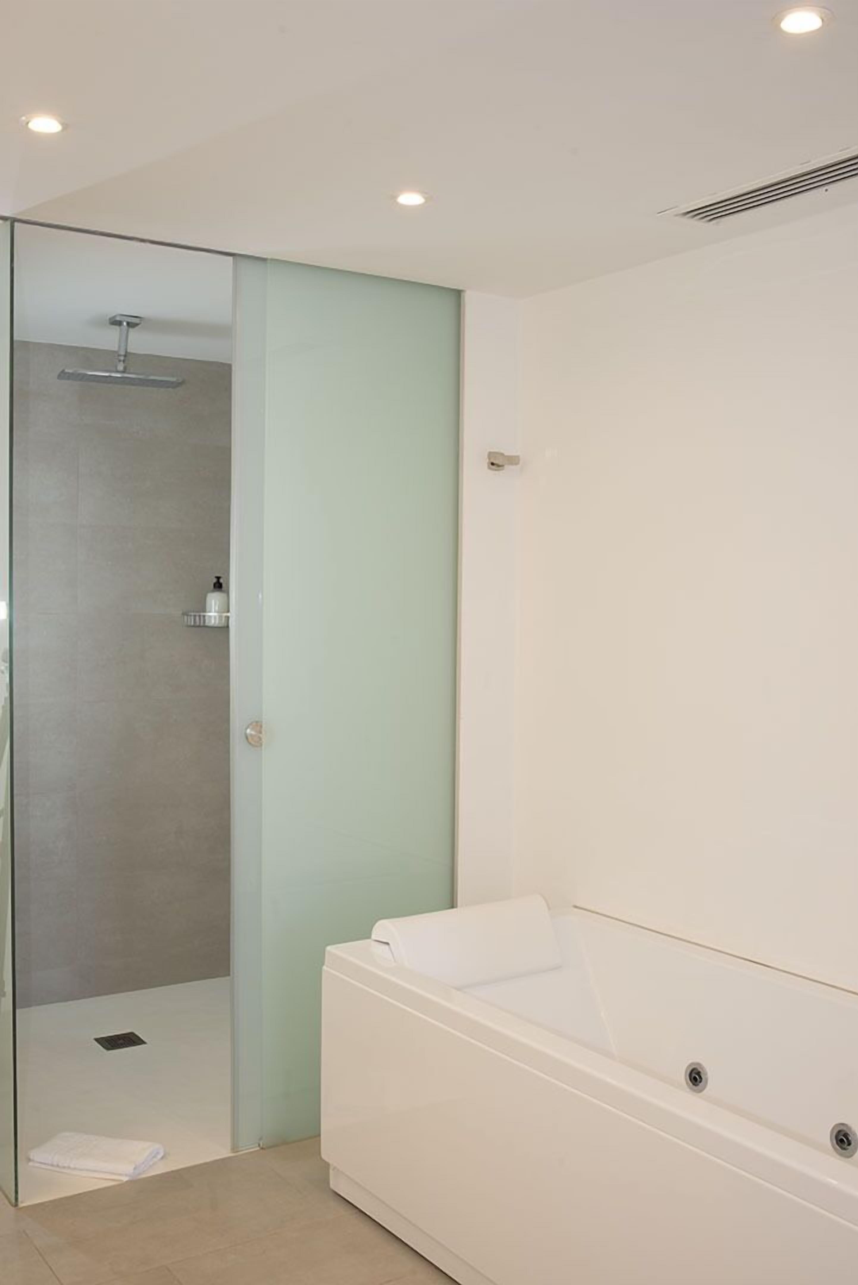 Een moderne badkamer met een douchecabine van glas, een witte badkuip en een lichtgroene wand.