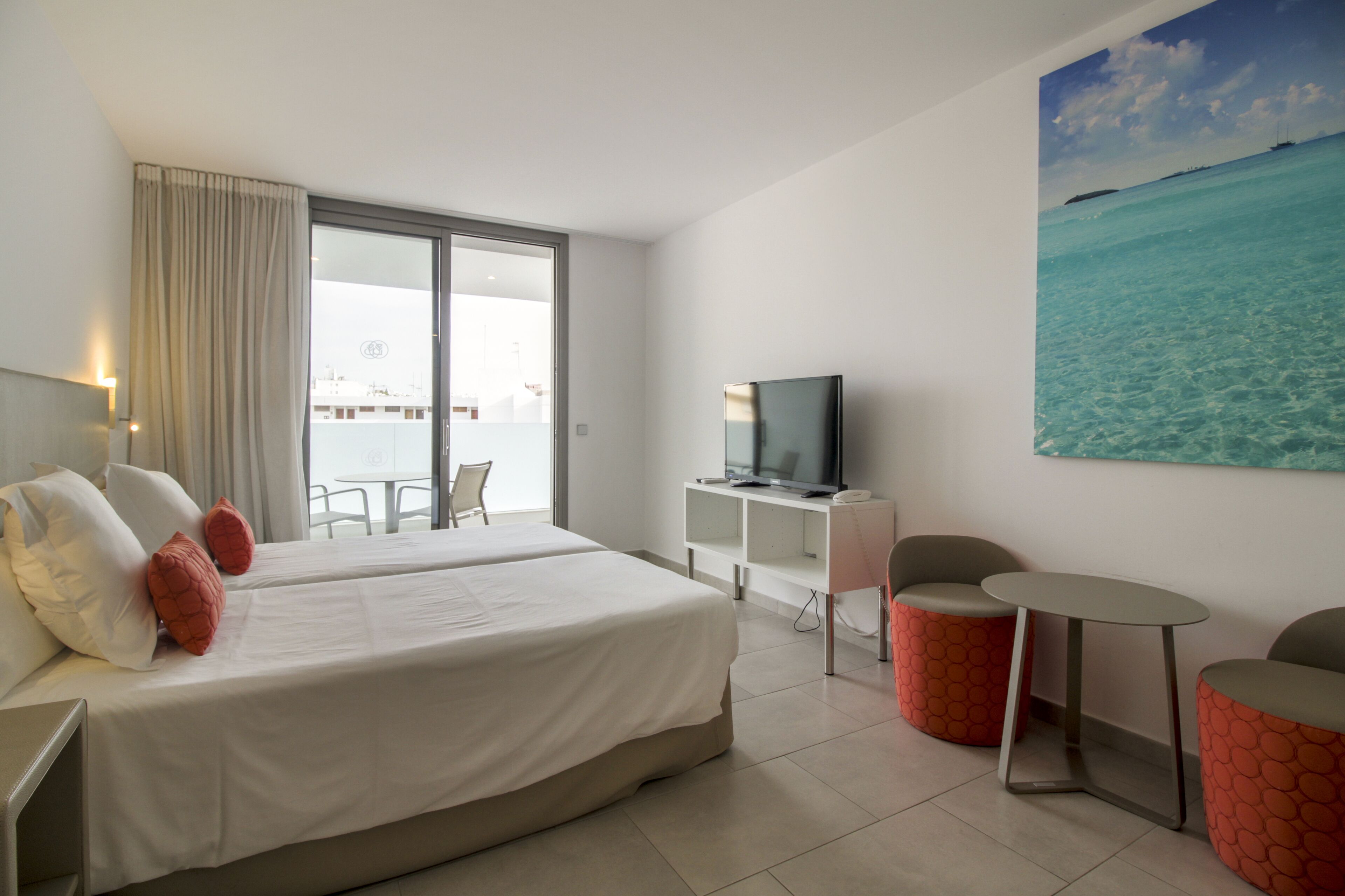 Ein Hotelzimmer mit einem großen Bett, einem Fernseher, einem Schreibtisch und einem Balkon mit Meerblick.