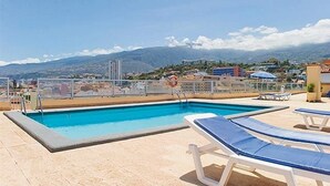 A rooftop pool with clear blue water, surrounded by lounge chairs and a view of distant mountains.