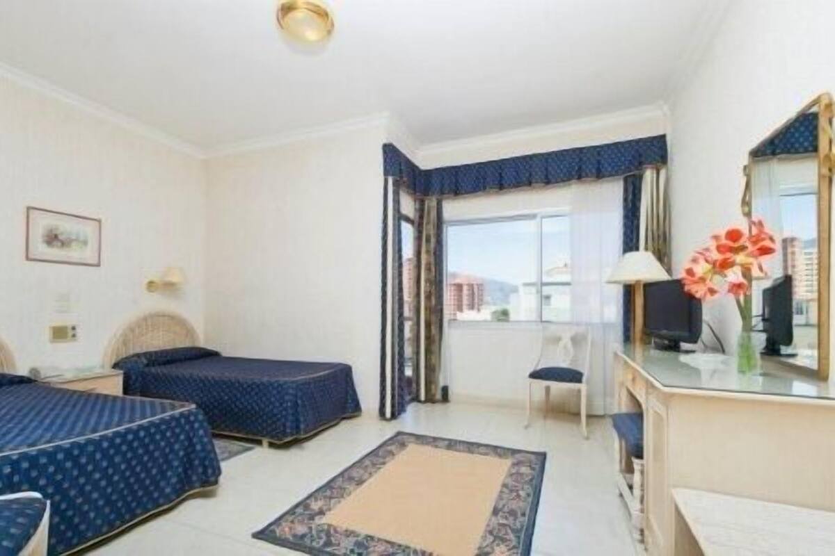 A hotel room with two beds, a desk, a chair, a TV, and a window with a view.
