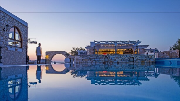A stone building with a 'Welcome' sign, a stone bridge, and a pool reflecting the architecture. - Contaratos Beach (Paros)