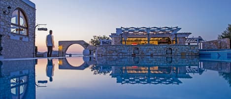 A stone building with a 'Welcome' sign, a stone bridge, and a pool reflecting the architecture.