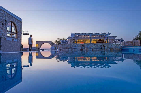 A stone building with a 'Welcome' sign, a stone bridge, and a pool reflecting the architecture. - Contaratos Beach (Paros)