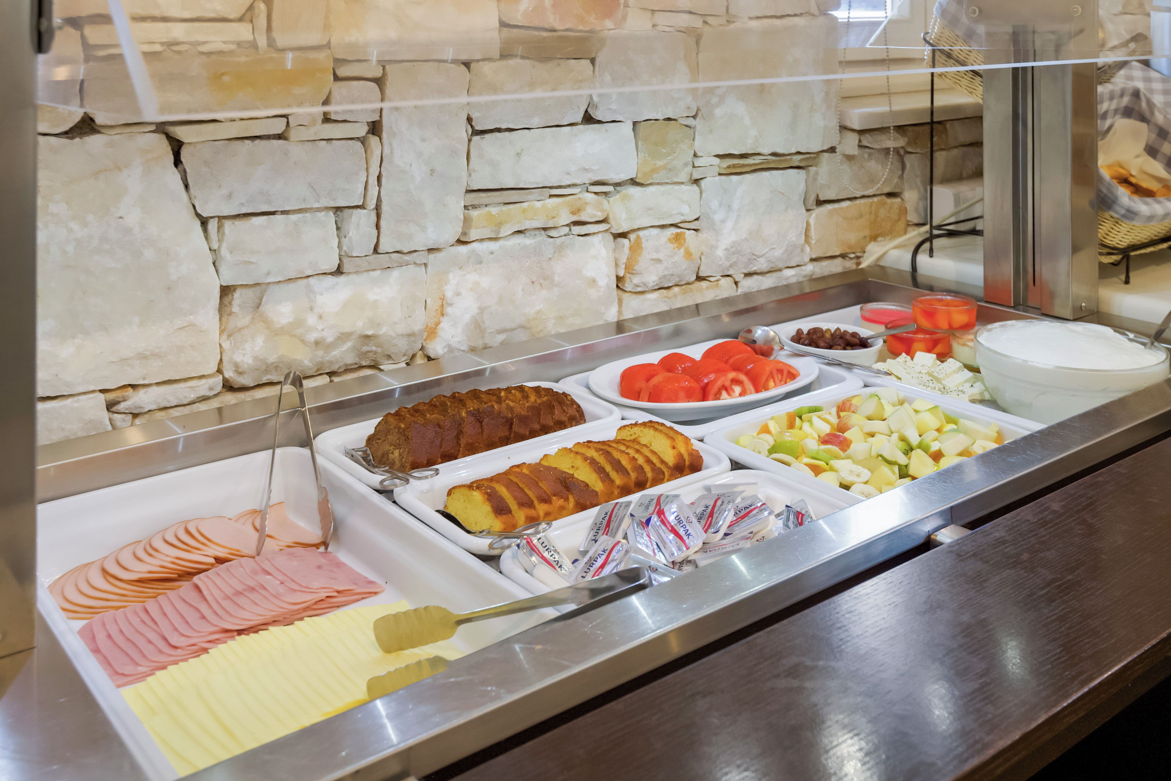 A buffet with various food items including sliced meats, a loaf of bread, and assorted fruits.