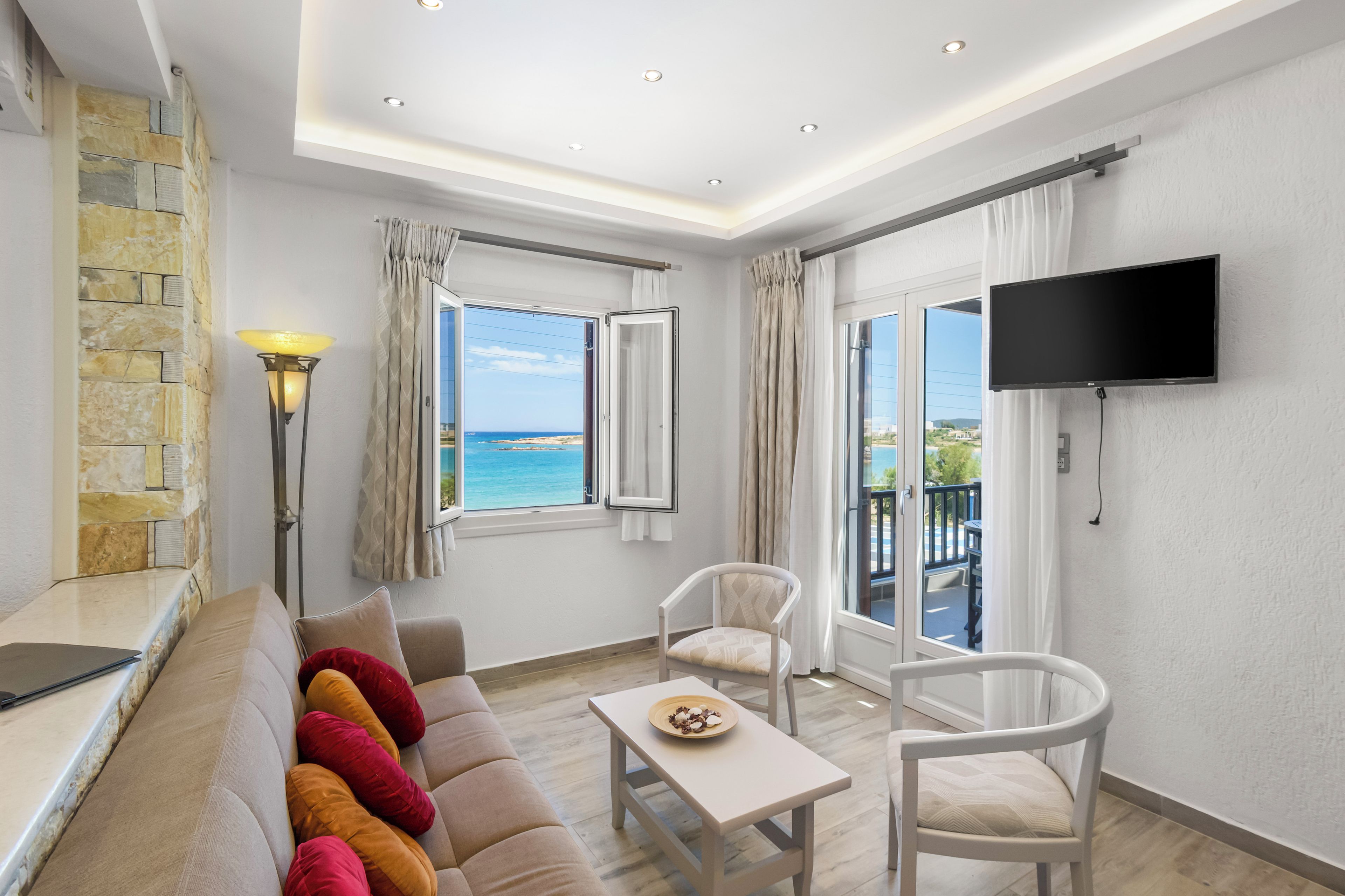 Un salon moderne avec un canapé, des fauteuils, une table, un téléviseur et une vue sur la mer.