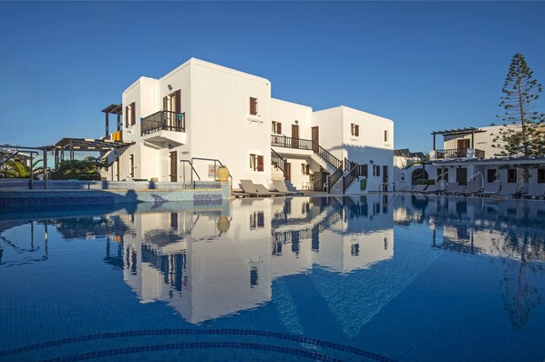 Una piscina que refleja un edificio blanco con balcones y escaleras.