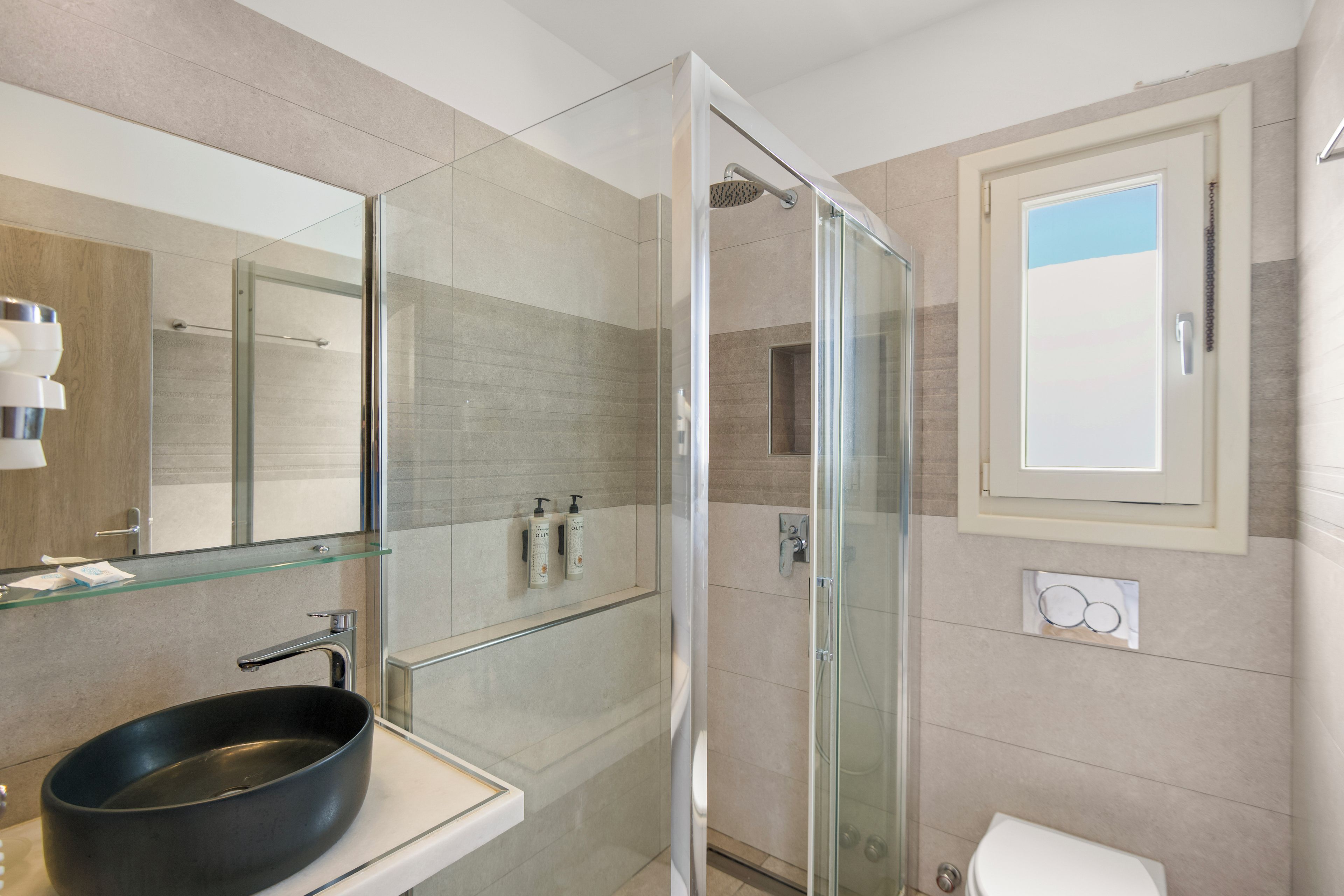 A modern bathroom with a glass-enclosed shower, a black basin sink, and a large mirror.