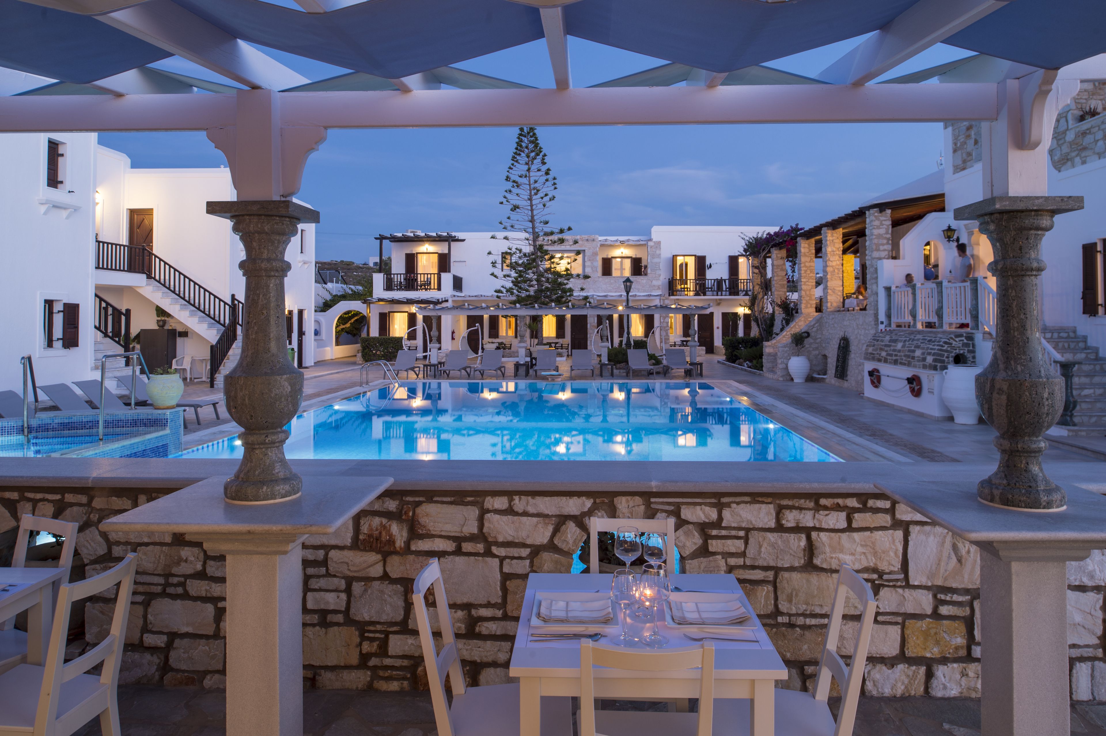 A poolside area with stone columns, a dining table set for two, and a staircase leading to upper levels.