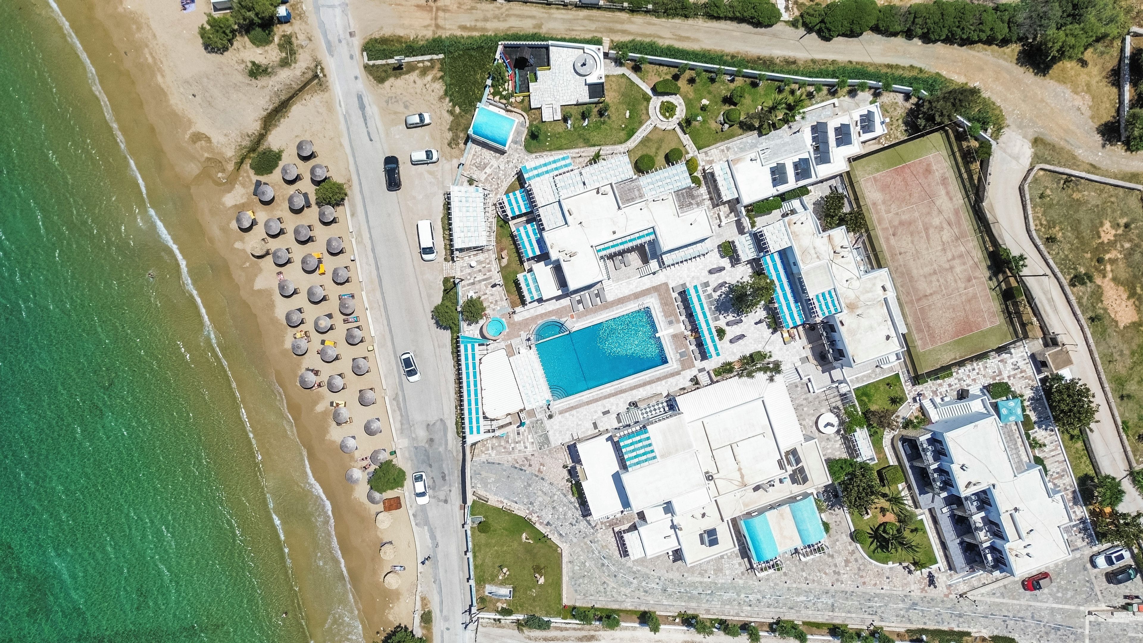Vista aérea de una propiedad costera con piscina, sombrillas de playa y un área de estacionamiento.