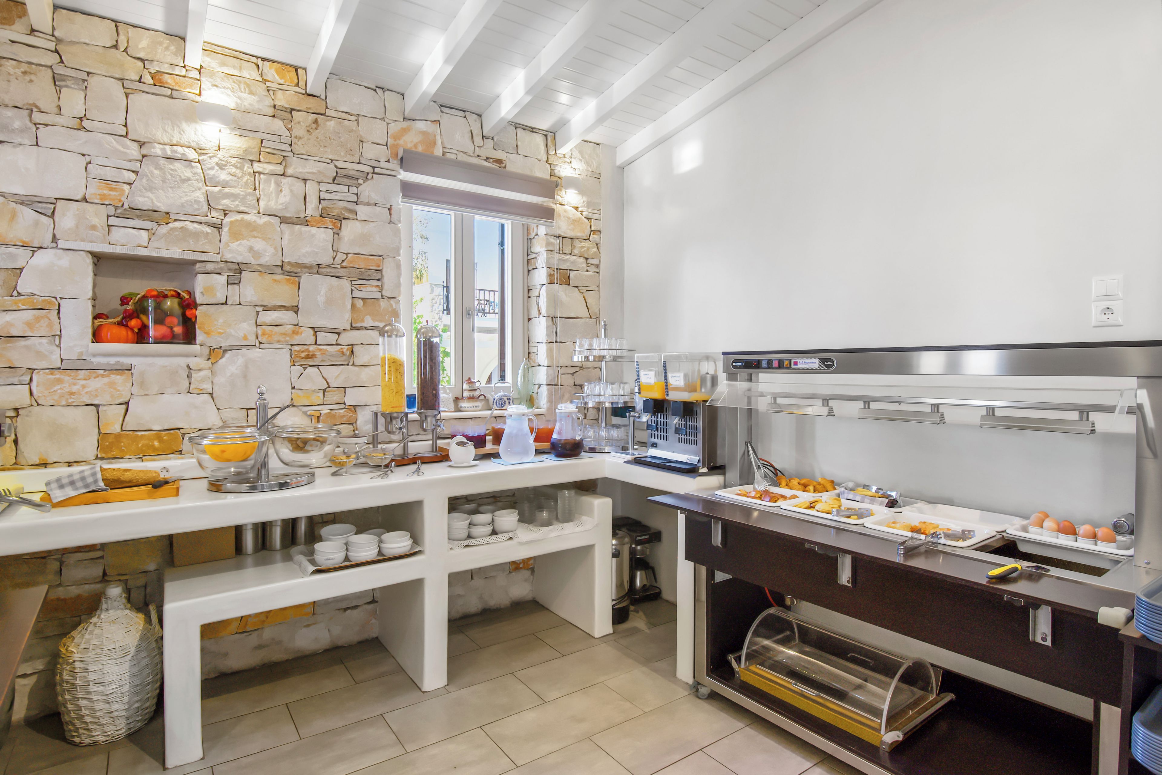 A breakfast buffet with a stone wall, a window, and various food and drink stations.