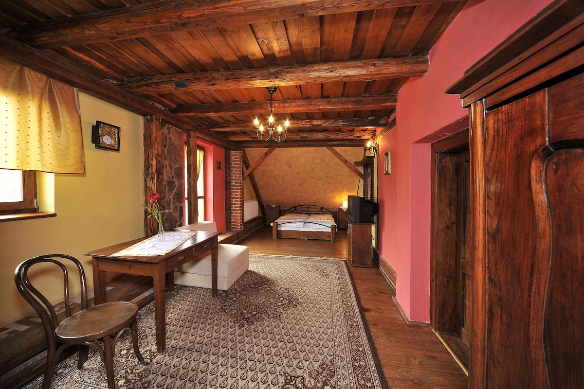 A cozy attic bedroom with a wooden ceiling, a bed, a desk, and a chair.