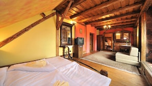 A room with a bed, a television, a wooden ceiling, and a dining area. - Apartmány Village (Velky Slavkov)