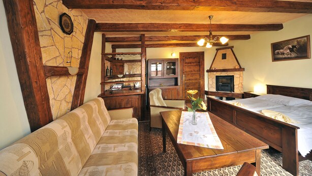 A rustic room with a stone wall, wooden beams, a sofa, a wooden table with a vase, and a bed. - Apartmány Village (Velky Slavkov)