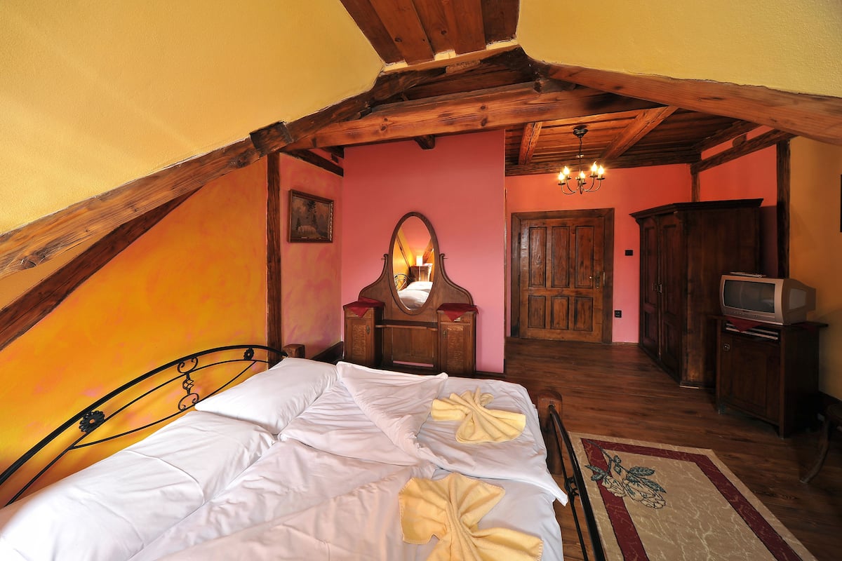 A bedroom with a wooden ceiling, a bed with white linens, a mirror, a wooden dresser, a television, and a rug.