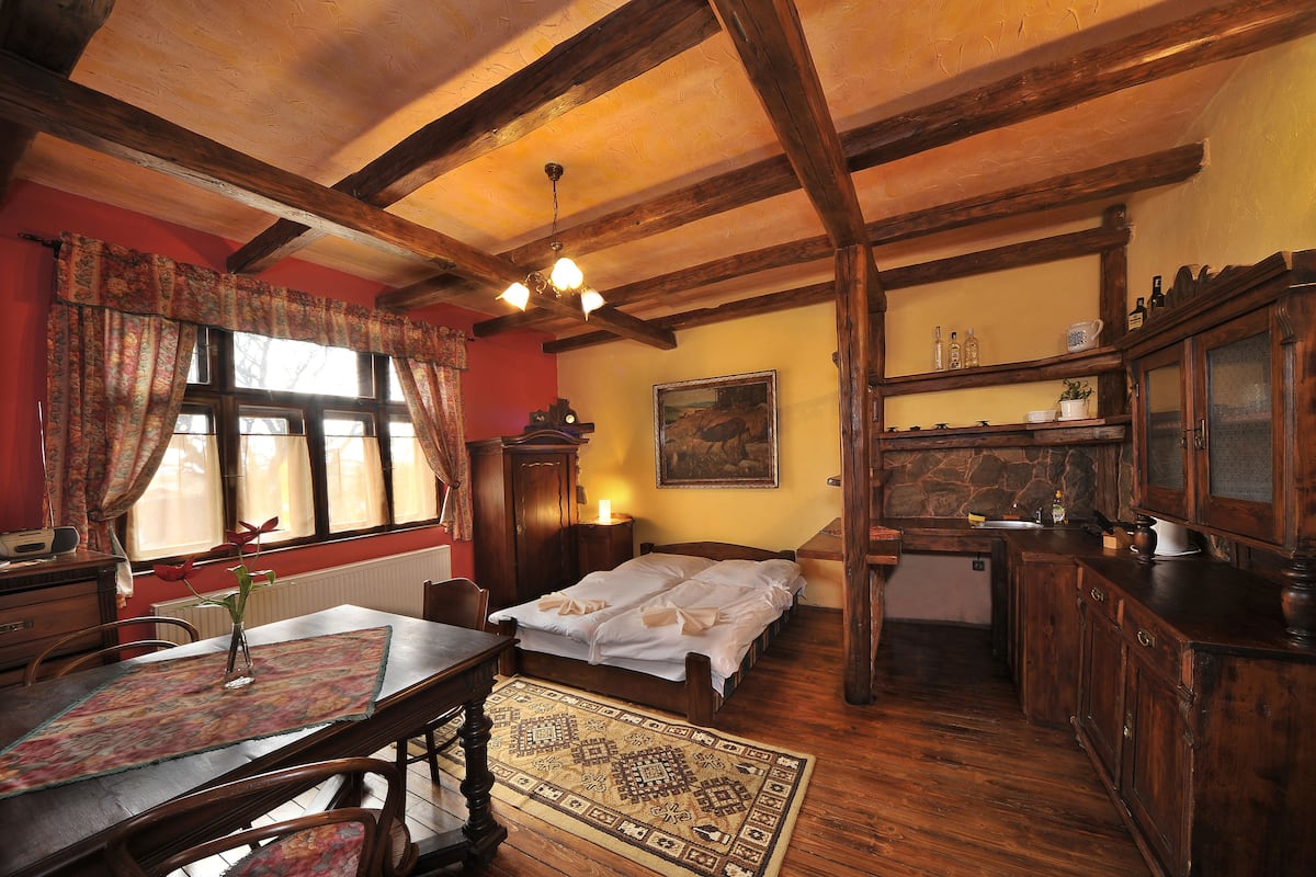 A traditional room with a wooden ceiling, a bed, a table with a placemat, and a window with curtains.