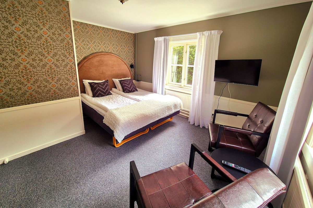 A hotel room with a bed, a TV, a chair, and a window with curtains.