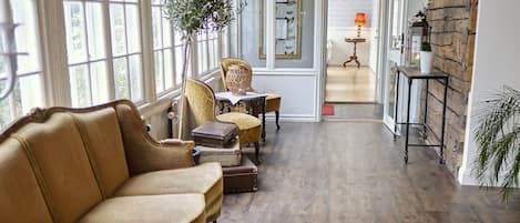 A spacious room with a wooden floor, large windows, and a cozy seating area with leather chairs and a small table.