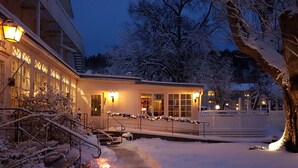 Ein schneebedecktes Gebäude mit einer Treppe, die zu einer Tür führt, einem überdachten Gang und einem Baum im Vordergrund.
