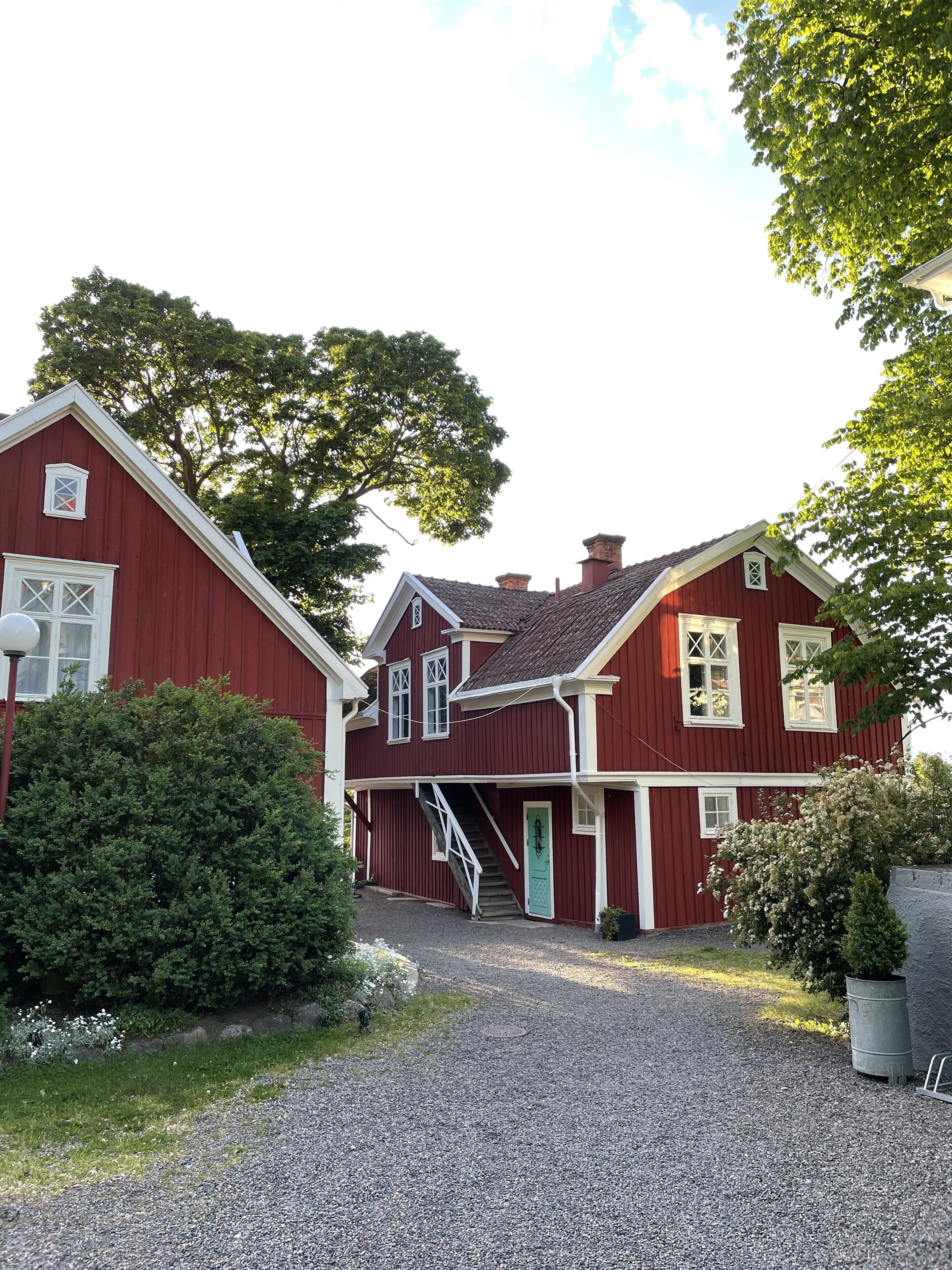 A red two-story house with a gravel driveway and a green door.