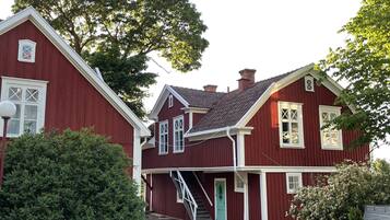 A red two-story house with a gravel driveway and a green door.