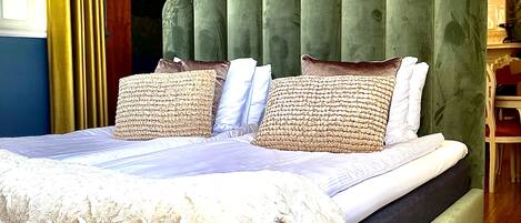 Une chambre à coucher avec un grand lit, une tête de lit recouverte d’un tissu vert, de nombreux oreillers et un luminaire décoratif au plafond.