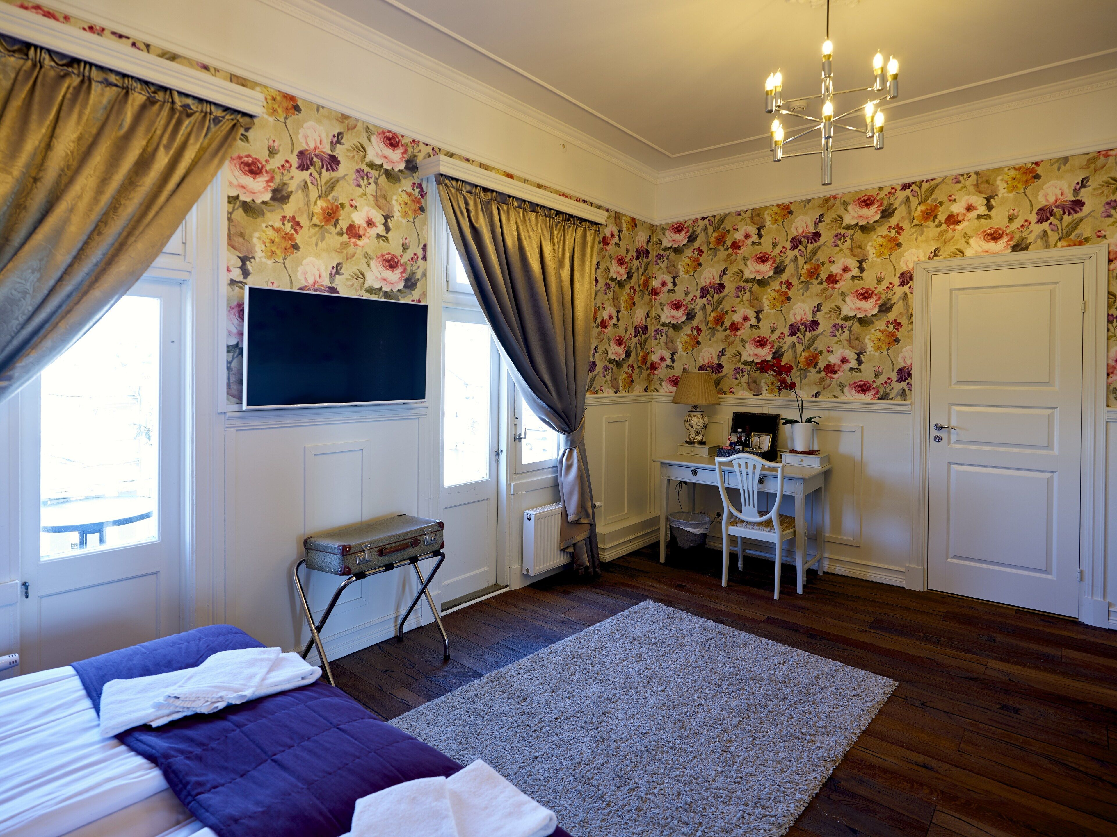 Un dormitorio con cama, escritorio, silla, radiador y ventana con cortinas.