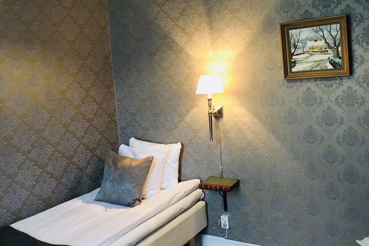 A bedroom with a bed, a nightstand, a lamp, a framed picture, and a chair.