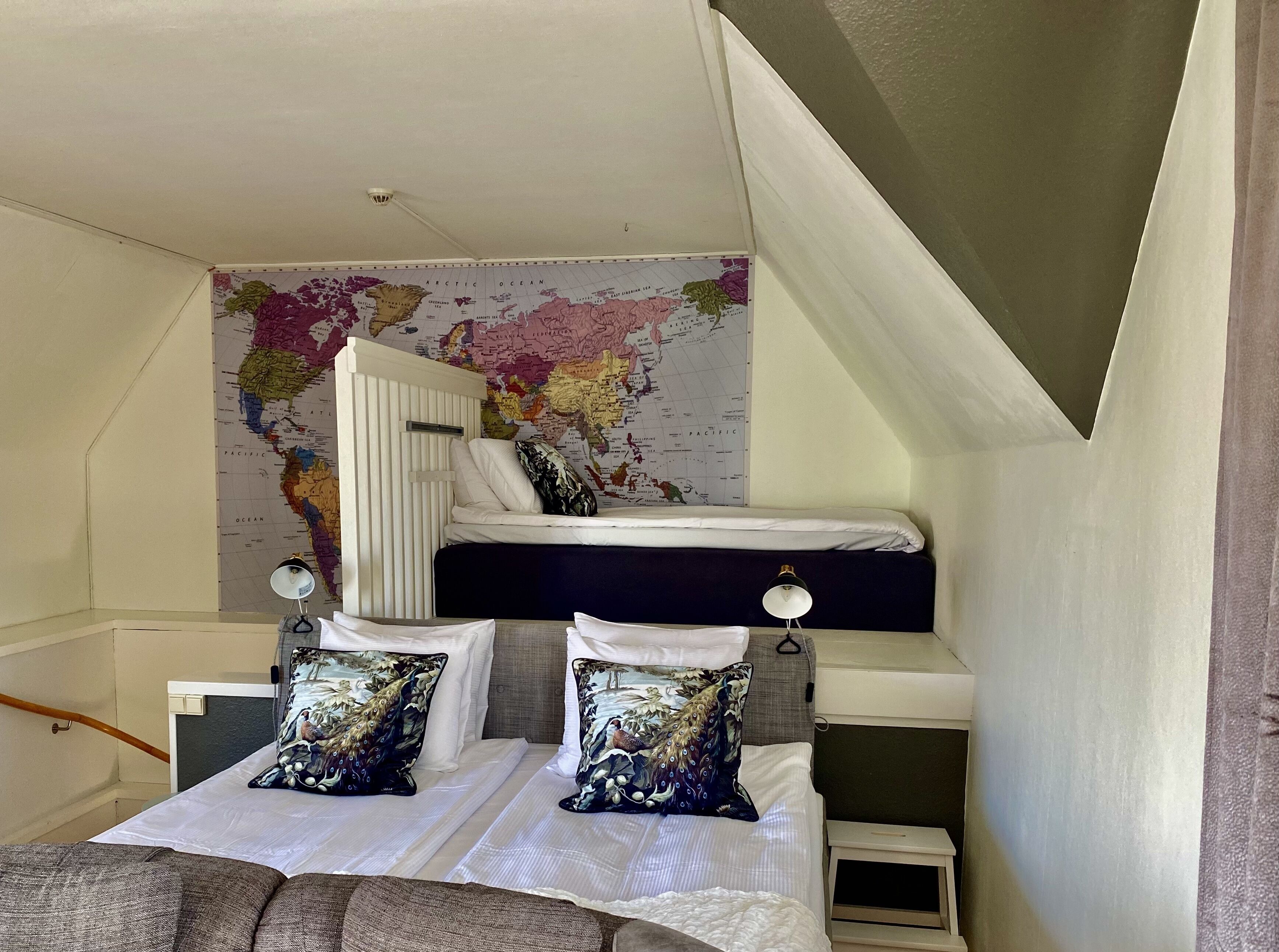 A dorm-style room with a bunk bed, a world map on the wall, and two bedside tables with lamps.