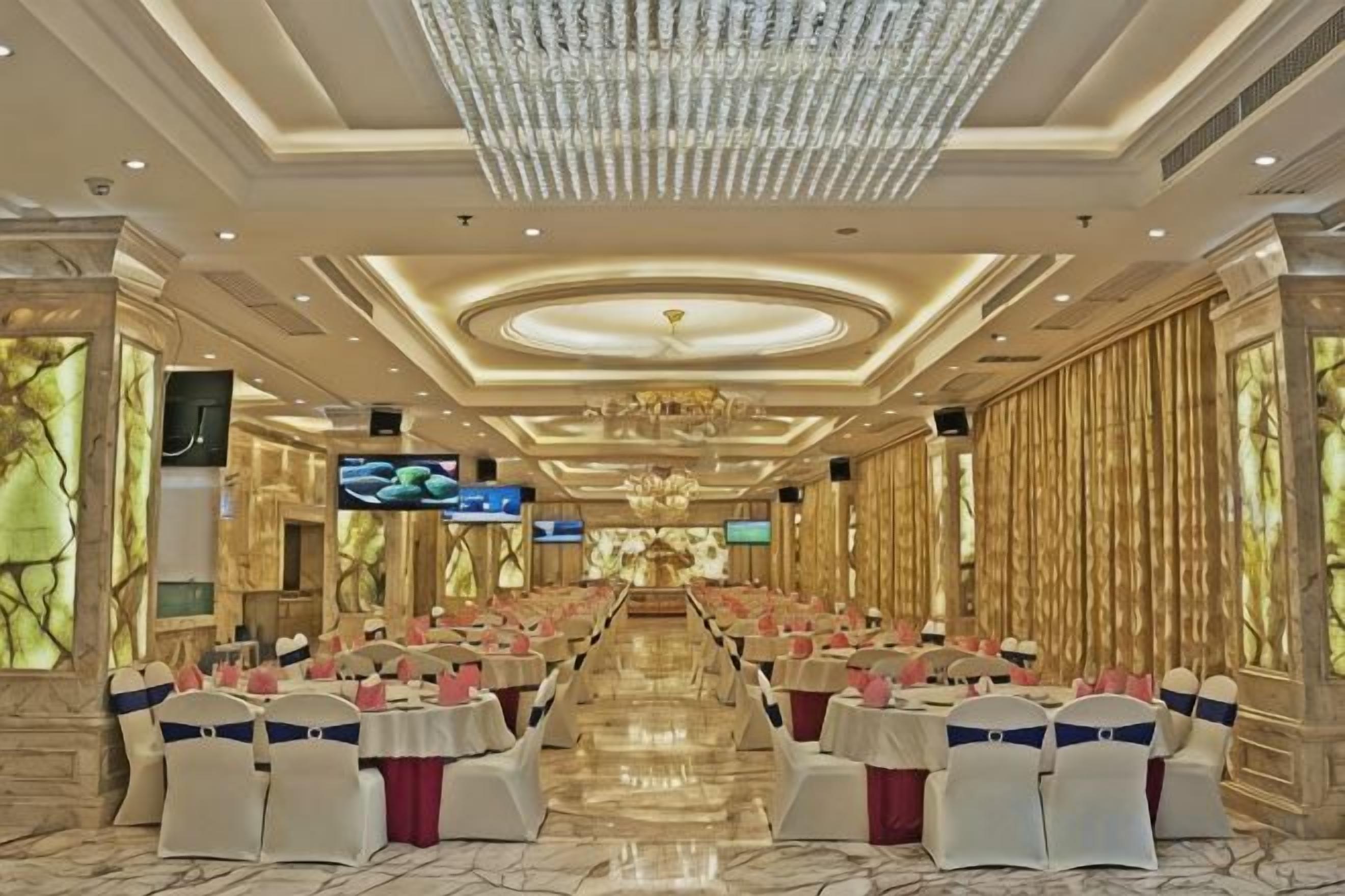 Un salón de banquetes con filas de mesas, una araña y una pantalla de televisión.