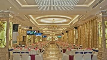 Un salón de banquetes con filas de mesas, una araña y una pantalla de televisión.