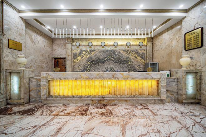 A marble reception desk with a clock, a framed plaque, and a decorative wall panel.