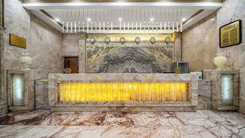 A marble reception desk with a clock, a framed plaque, and a decorative wall panel.