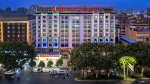 Ein mehrstöckiges Hotel mit auffälliger Beschilderung, umgeben von Bäumen und einer belebten Straße.